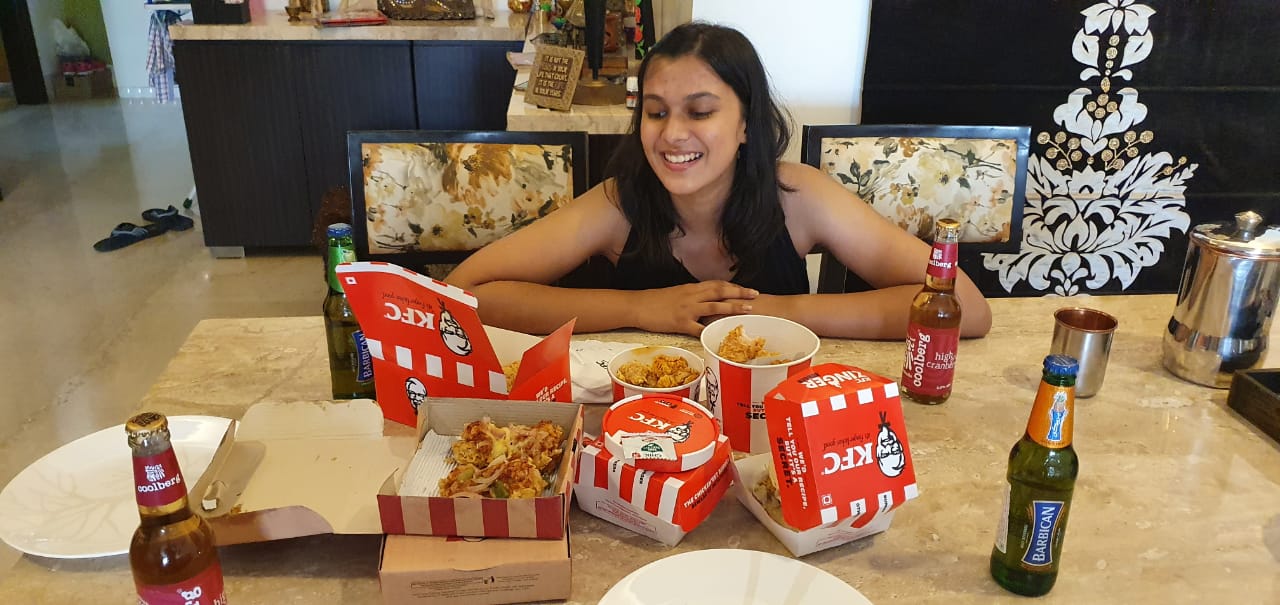 Aarushi grinning down at a table spread with buckets and boxes of fried chicken.