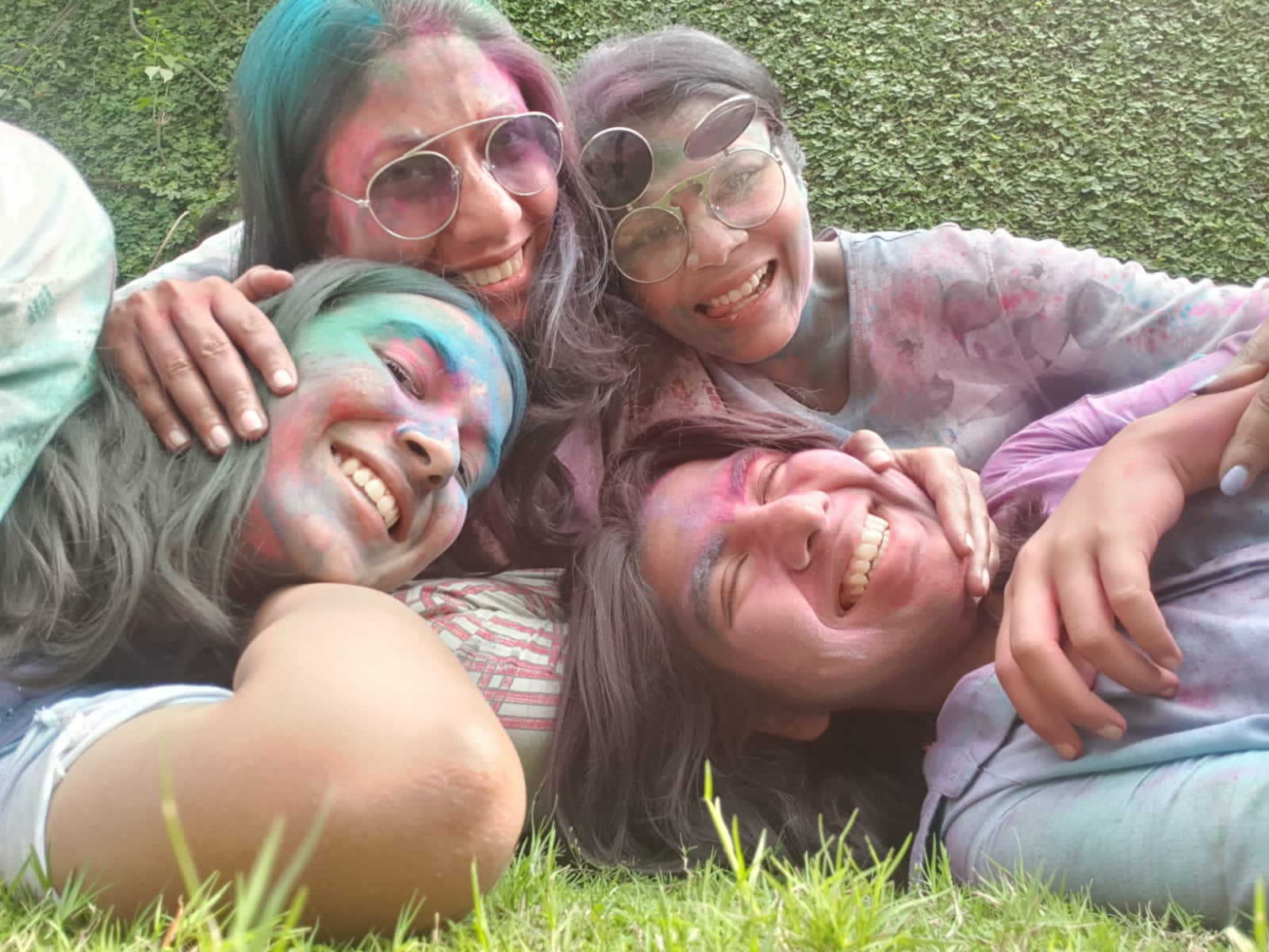 Aarushi with three of the women in her family lying together on the grass at Holi, faces bright with colour, all laughing.