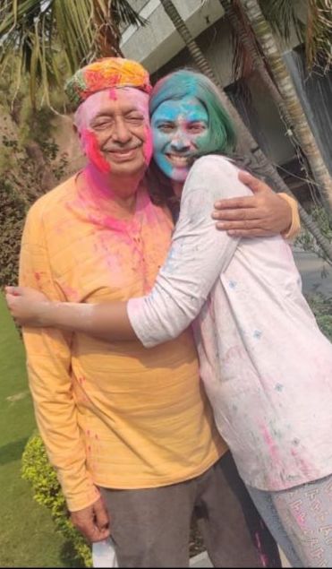 Aarushi hugging her grandfather at Holi, both of their faces covered in bright colour, smiling.