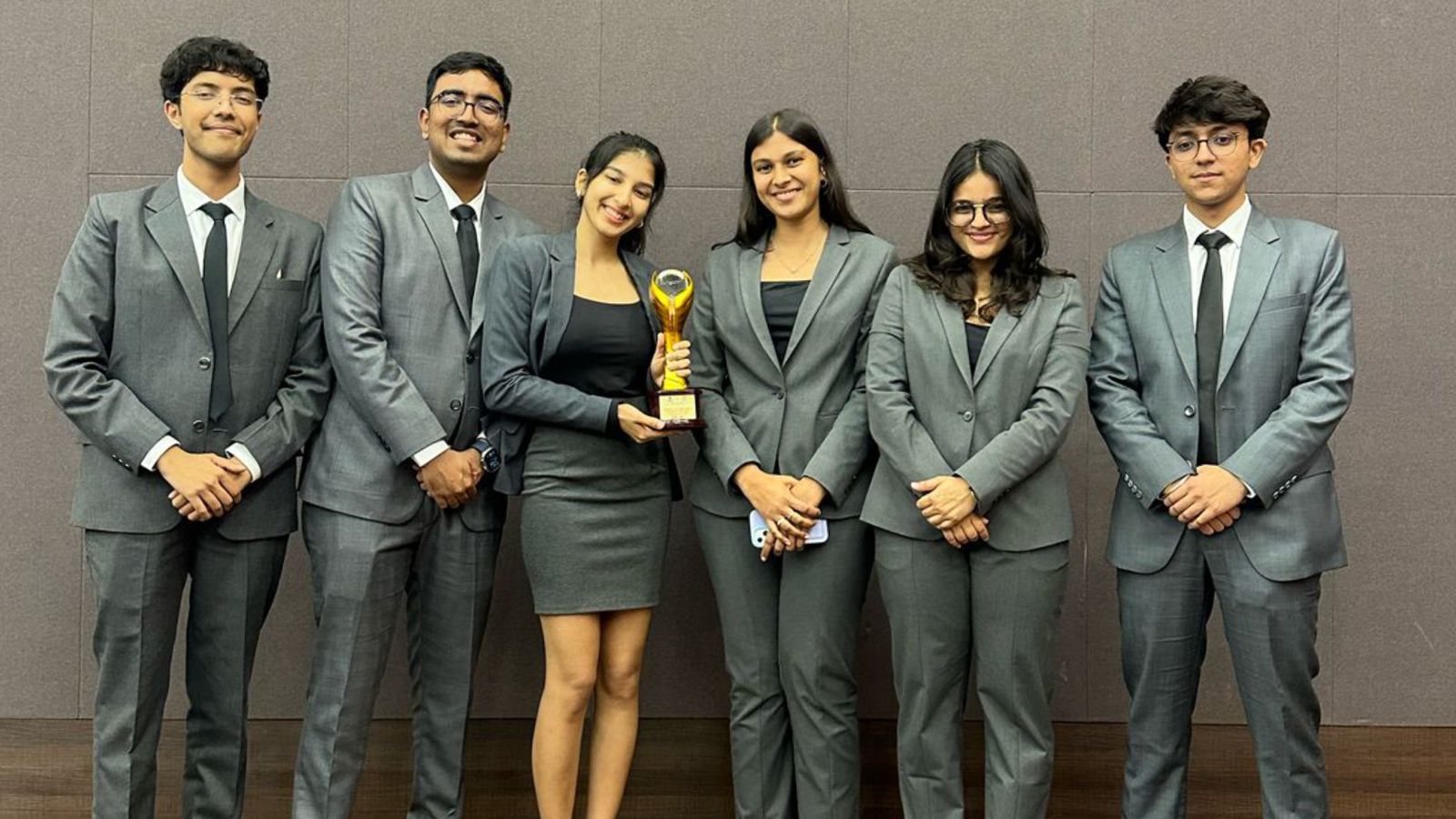 Aarushi holding a gold trophy with her team, all in grey suits, after winning the moot.